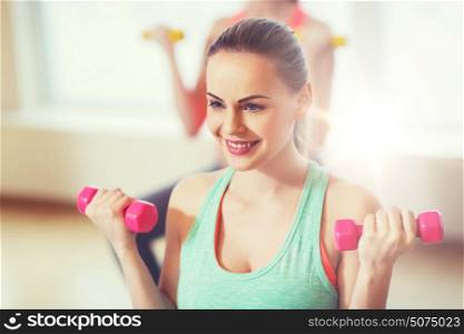 fitness, sport, training and lifestyle concept - happy smiling young woman with dumbbells exercising in gym. smiling woman with dumbbells exercising in gym