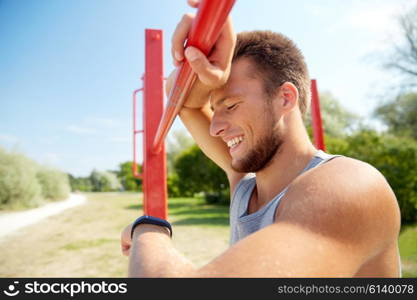 fitness, sport, training and lifestyle concept - happy young man looking at heart-rate watch bracelet and exercising on horizontal bar outdoors