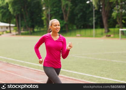 fitness, sport, training and lifestyle concept - smiling african american woman running on track outdoors