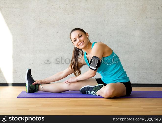 fitness, sport, training and lifestyle concept - smiling woman stretching leg on mat in gym