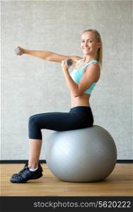 fitness, sport, training and lifestyle concept - smiling woman with dumbbells and exercise ball in gym