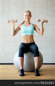 fitness, sport, training and lifestyle concept - smiling woman with dumbbells and exercise ball in gym