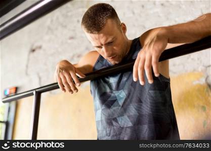 fitness, sport, training and lifestyle concept - tired young man exercising on parallel bars in gym. tired young man at parallel bars in gym