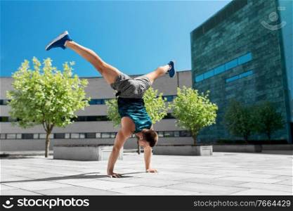 fitness, sport, training and lifestyle concept - young man exercising and doing handstand with split legs outdoors. young man exercising and doing handstand outdoors
