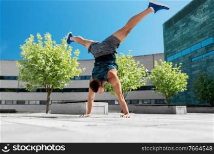 fitness, sport, training and lifestyle concept - young man exercising and doing handstand with split legs outdoors. young man exercising and doing handstand outdoors