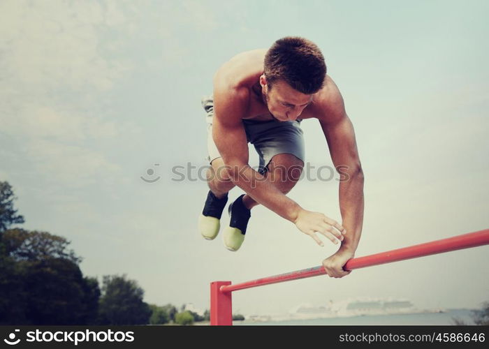 fitness, sport, training and lifestyle concept - young man exercising on horizontal bar outdoors