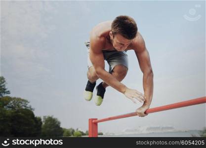fitness, sport, training and lifestyle concept - young man exercising on horizontal bar outdoors