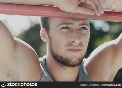 fitness, sport, training and lifestyle concept - young man exercising on horizontal bar outdoors