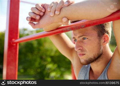 fitness, sport, training and lifestyle concept - young man exercising on horizontal bar outdoors