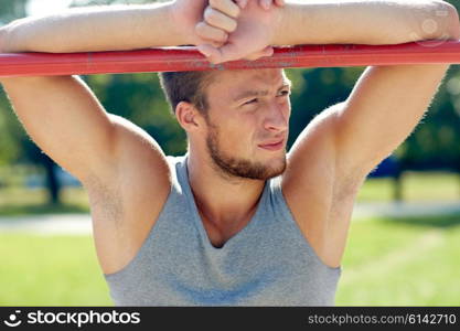 fitness, sport, training and lifestyle concept - young man exercising on horizontal bar outdoors