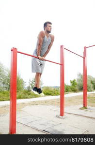 fitness, sport, training and lifestyle concept - young man exercising on horizontal bar outdoors