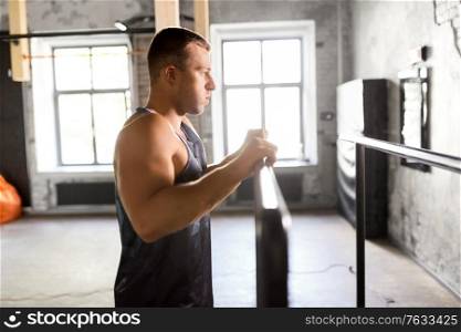 fitness, sport, training and lifestyle concept - young man exercising on parallel bars in gym. young man at parallel bars in gym