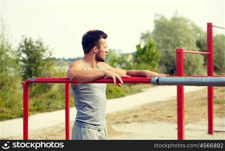 fitness, sport, training and lifestyle concept - young man exercising on parallel bars outdoors