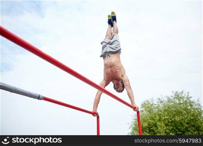 fitness, sport, training and lifestyle concept - young man exercising on parallel bars outdoors