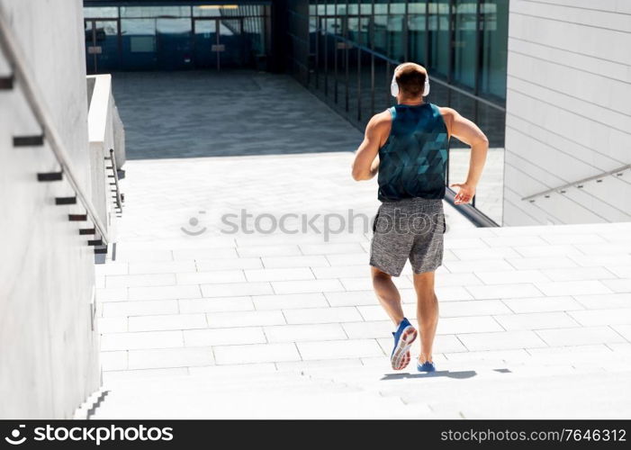 fitness, sport, training and lifestyle concept - young man in headphones running downstairs outdoors. young man in headphones running downstairs