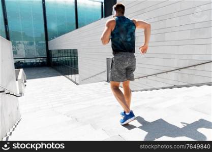fitness, sport, training and lifestyle concept - young man in headphones running downstairs outdoors. young man in headphones running downstairs
