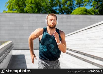 fitness, sport, training and lifestyle concept - young man in headphones running outdoors. young man in headphones running outdoors