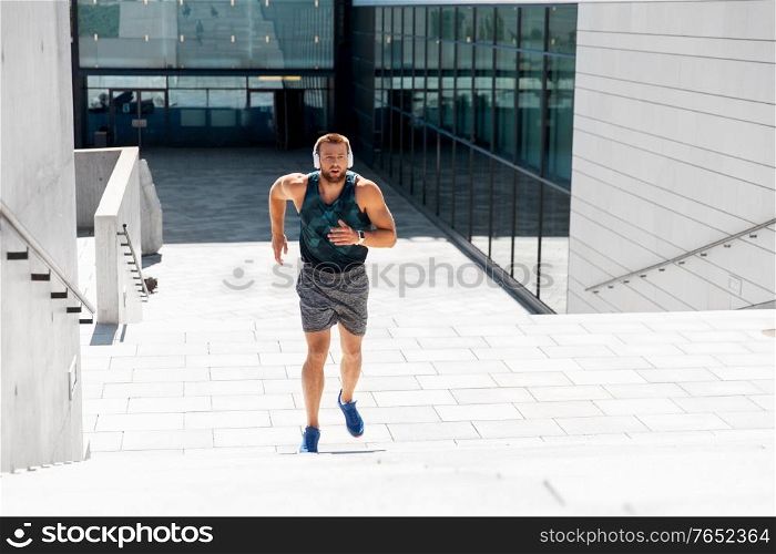 fitness, sport, training and lifestyle concept - young man in headphones running upstairs outdoors. young man in headphones running upstairs outdoors