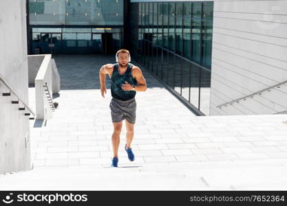 fitness, sport, training and lifestyle concept - young man in headphones running upstairs outdoors. young man in headphones running upstairs outdoors