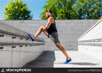 fitness, sport, training and lifestyle concept - young man in headphones stretching leg outdoors. young man in headphones stretching leg outdoors