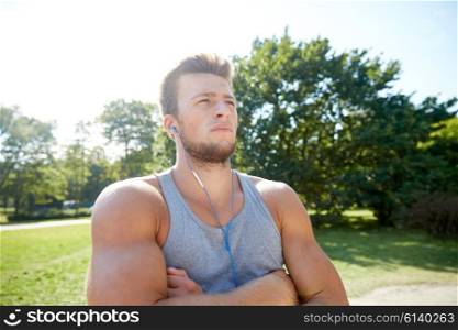 fitness, sport, training and lifestyle concept - young man with earphones listening to music at summer park