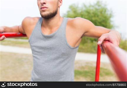 fitness, sport, training and people concept - close up of young man exercising on parallel bars outdoors