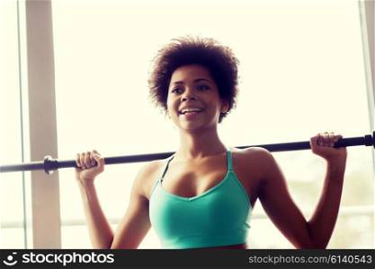 fitness, sport, training and people concept - happy smiling african american woman holding bar in gym