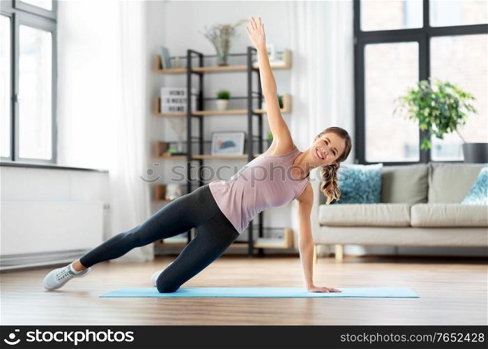 fitness, sport, training and people concept - happy smiling young woman doing side plank exercise on mat at home. happy woman doing plank exercise on mat at home