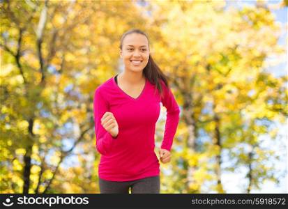 fitness, sport, training and people concept - smiling african american woman running outdoors over autumn trees background