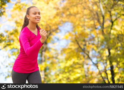 fitness, sport, training and people concept - smiling african american woman running outdoors over autumn trees background