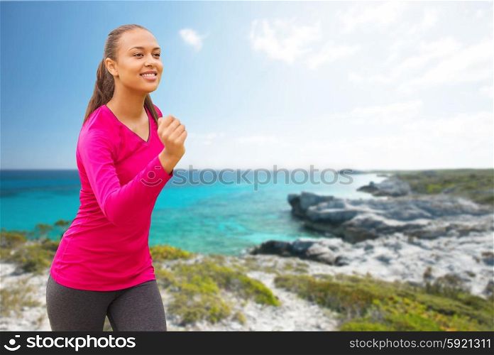 fitness, sport, training and people concept - smiling african american woman running outdoors over beach background