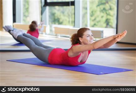 fitness, sport, training and people concept - smiling woman doing back extension exercise on mat in gym