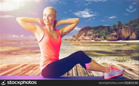fitness, sport, training and people concept - smiling woman exercising on mat outdoors over exotic tropical beach background. smiling woman exercising on mat outdoors