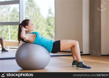 fitness, sport, training and people concept - smiling woman flexing abdominal muscles with exercise ball in gym