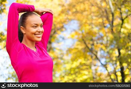 fitness, sport, training and people concept - smiling woman stretching hand over autumn park background