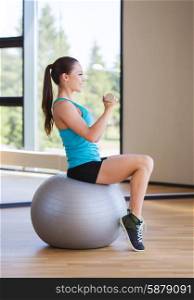 fitness, sport, training and people concept - smiling woman with dumbbells and exercise ball flexing muscles in gym