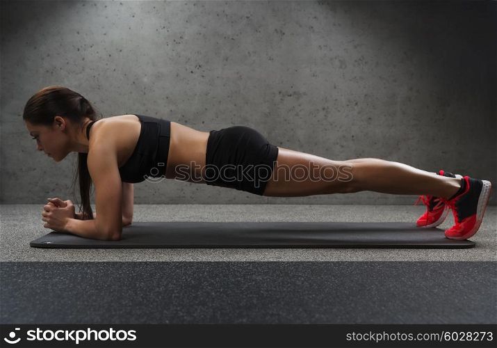 fitness, sport, training and people concept - woman doing plank exercise on mat in gym