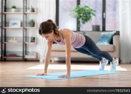 fitness, sport, training and people concept - young woman doing high plank exercise on mat at home. young woman doing plank exercise on mat at home