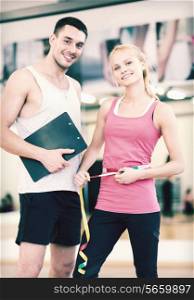 fitness, sport, training, diet and lifestyle concept - two smiling people with clipboard and measure tape in the gym