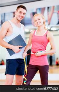 fitness, sport, training, diet, gym and lifestyle concept - two smiling people with clipboard and measure tape in the gym