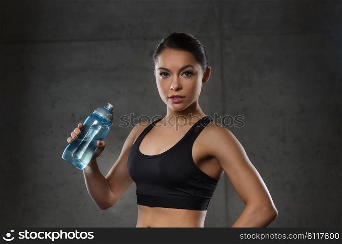 fitness, sport, training, drink and lifestyle concept - woman drinking water from bottle in gym