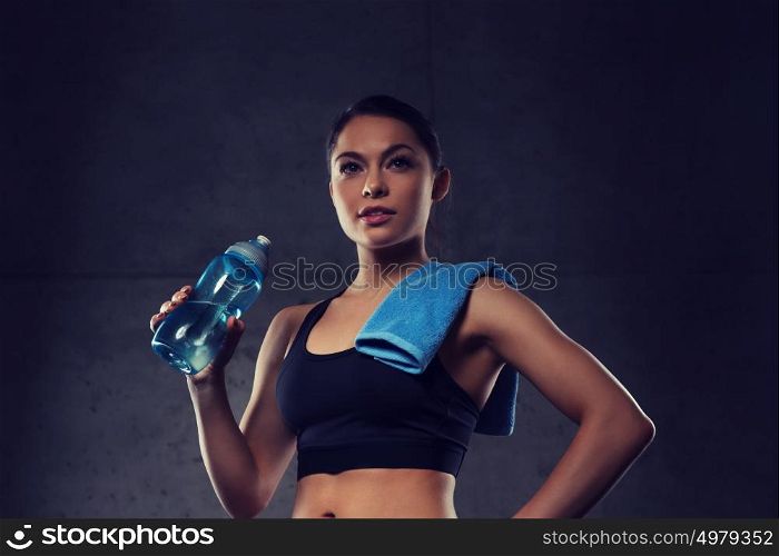fitness, sport, training, drink and lifestyle concept - woman with towel drinking water from bottle in gym. woman with towel drinking water from bottle in gym