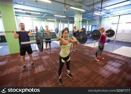 fitness, sport, training, exercising and lifestyle concept - group of people with barbells doing standing shoulder press in gym. group of people training with barbells in gym