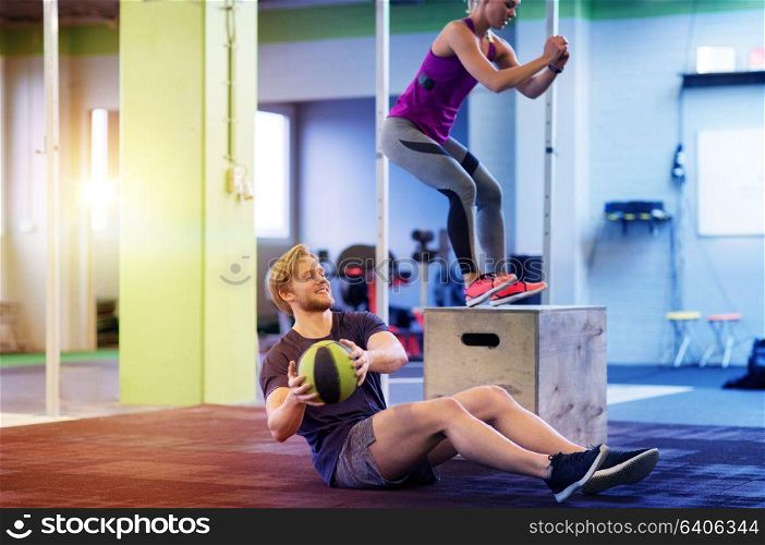 fitness, sport, training, exercising and people concept - happy woman and man with medicine ball doing curl ups and box jumps in gym. woman and man with medicine ball exercising in gym