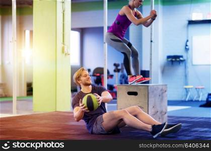 fitness, sport, training, exercising and people concept - happy woman and man with medicine ball doing curl ups and box jumps in gym. woman and man with medicine ball exercising in gym