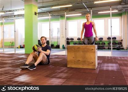fitness, sport, training, exercising and people concept - man and woman with medicine ball ready to do curl ups and box jumps in gym. man and woman ready to do workout
