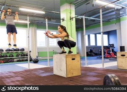 fitness, sport, training, exercising and people concept - woman and man doing pull-ups and box jumps in gym. woman and man exercising in gym. woman and man exercising in gym