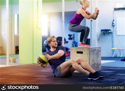 fitness, sport, training, exercising and people concept - woman and man with medicine ball doing curl ups and box jumps in gym. woman and man with medicine ball exercising in gym