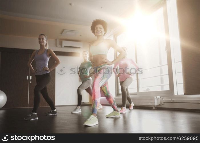 fitness, sport, training, gym and lifestyle concept - group of happy women working out and stretching leg in gym