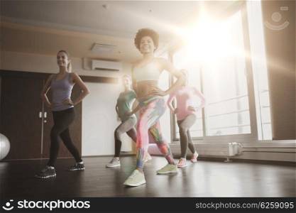fitness, sport, training, gym and lifestyle concept - group of happy women working out and stretching leg in gym